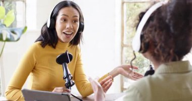 Çok ırklı kadın meslektaşlar evde kulaklıklar ve mikrofonla podcast yapıyorlar. podcast, yayıncılık, yardımcı sunucu, ev stüdyosu, içerik oluşturma, ses.