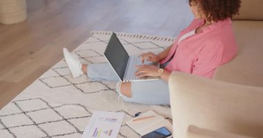 Yerde oturuyor, dizüstü bilgisayar kullanıyor ve evde oturma odasında çalışıyor. Uzaktan çalışma, ev ofisi, teknoloji, telekomünikasyon, serbest çalışma, üretkenlik