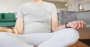 Evde meditasyon yaparken, oturma odasında yoga minderleri üzerinde bağdaş kuran çok ırklı yaşlı bir çift. Sağlık, rahatlama, farkındalık, meditasyon, fitness, yaşam tarzı