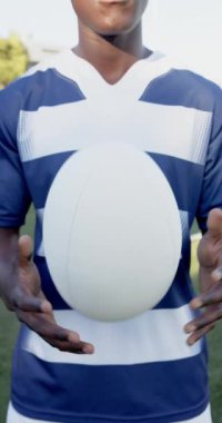 Dikey video: Rugby oyuncusu topu sahada tutuyor, mavi-beyaz forma giyiyor. Spor, atlet, yarışma, takım, açık hava, üniforma