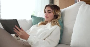 Kanepede dinlenmek, evde tablet kullanan bir kadın, boş vakitlerin tadını çıkarmak. Rahatlama, teknoloji, yaşam tarzı, konfor, dijital, gelişigüzel