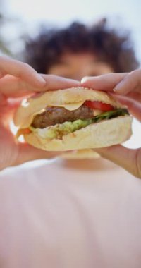 Dikey video: Açık havada sulu burger tutmak, taze malzemeli sandviçin tadını çıkaran insanlar. Lezzetli, lezzetli, fast food, yaşam tarzı, yemek, piknik