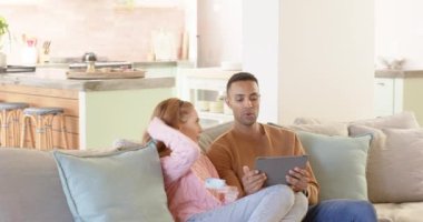 Kanepede dinlenen bir çift, online alışveriş için tablet ve kredi kartı kullanıyorlar. E-ticaret, rahatlama, yaşam tarzı, dijital, teknoloji, internet