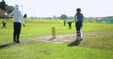 Kriket oyuncuları güneşli sahada kalelerin arasında koşuyor, takım çalışmasına odaklanıyor. Spor, sporcular, rekabet, işbirliği