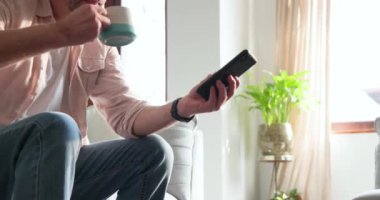 Evde elinde akıllı telefonla kahve bardağına uzanan kıdemli bir adam var. Teknoloji, yaşam tarzı, yaşlılar, iletişim, çoklu görev, rahatlama