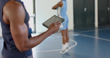 Koç tablet tutuyor, basketbol oyuncusunu spor salonunda salya akıtırken izliyor. koçluk, eğitim, teknoloji, atlet, takım çalışması, fitness