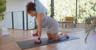 Yoga minderinde egzersiz yapan, evde egzersiz yaparken dambılları kaldıran bir kadın. Spor, egzersiz, ağırlık, antrenman, sağlıklı yaşam tarzı, spor salonu