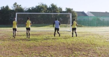 Sahada futbol oynuyorlar, erkekler kale direğinin yanında yarışıyor ve savunuyorlar. Spor, rekabet, takım çalışması, atletik, oyun