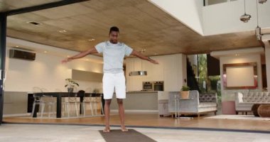 Yoga pratiği yapan, modern oturma odasında yoga minderinin üzerinde duran Afro-Amerikan bir adam. Meditasyon, fitness, sağlık, egzersiz, ev çalışması, rahatlama