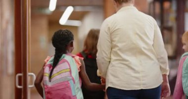 Okul koridorunda yürürken, kadın öğretmen sırt çantalı öğrencinin elini tutuyor. Eğitim, akıl hocalığı, öğrenme, rehberlik, destek