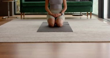 Yoga minderinde diz çökmek, kadının evde meditasyon yapması ve dinlenmesi. Sağlık, fitness, spiritüellik, farkındalık, rahatlama, kapalı alan