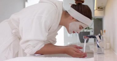 Yüzünü temizleyiciyle yıkamak, bornozlu bir kadının evde cilt bakımını yapması. Güzellik, kişisel bakım, hijyen, sağlık, bakım, banyo.