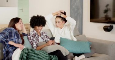 Kadın arkadaşlar kanepede dinleniyor, birlikte akıllı telefona bakarken kahkahalar atıyorlar. Arkadaşlık, bağlanma, eğlence, teknoloji, rahatlama, rahatlama.