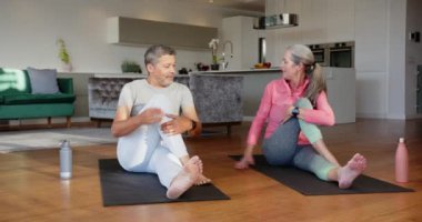 Yoga yapıyor, çok ırklı son sınıf çifti oturma odasında yoga minderlerini eğip büküyor. Zindelik, sağlık, ev, egzersiz, esneklik, meditasyon