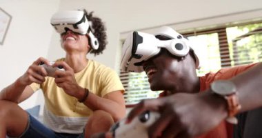 Video oyunları oynuyorlar, iki çok ırklı erkek arkadaş evde video kulaklık ve kumanda kullanıyorlar. Oyun, teknoloji, çok ırklı erkek arkadaşlar, sanal gerçeklik, eğlence, eğlence