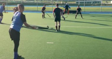 Çim hokeyi oynuyorlar, erkekler güneşli bir günde açık hava maçında yarışıyorlar. Spor, rekabet, takım çalışması, açık hava, oyuncular, aksiyon