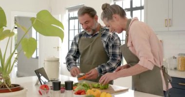 Olgun çift mutfakta birlikte yemek pişiriyor, tarif rehberliği için tablet kullanıyorlar. Yaşlılar, yaşam tarzı, teknoloji, bağlanma