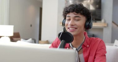 Kulaklık takıyor, transseksüel ergen çocuk gülümsüyor ve evde podcast kaydediyor. Podcast, ev stüdyosu, yayın, ses, mikrofon, yaşam tarzı