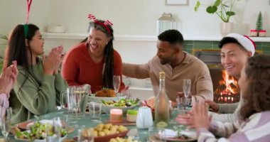 Çeşitli aileler Noel yemeğini birlikte kutluyor, şöminenin yanında neşe ve kahkaha paylaşıyor. Kutlama, tatil, toplanma, şenlik, sıcaklık, gelenek