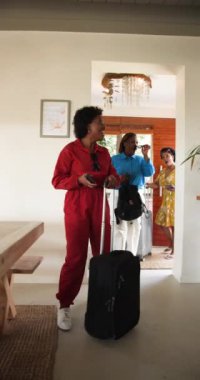 Dikey video: Afro-Amerikalı kadınlar bavullarıyla geliyorlar, gülüyorlar ve tatilin tadını çıkarıyorlar. Seyahat, arkadaşlık, kahkaha, tatil, kutlama, mutluluk