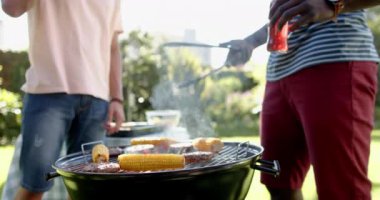 Izgarada mısır ve burger ızgara, dışarıda takılmaktan hoşlanan iki çok ırklı erkek arkadaş. Yaz, yemek, arkadaşlar, yemek, eğlence, sosyal