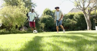 Futbol oynuyorlar, iki çok ırklı erkek arkadaş güneşli bir parkta fotokopi çekiyorlar. Spor, eğlence, spor, spor, açık hava, takım çalışması, aktif yaşam tarzı