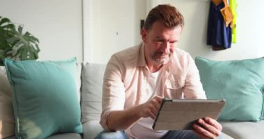 Kıdemli adam evde tablet kullanıyor, gülümsüyor ve teknolojinin tadını çıkarıyor. Yaşlılar, mutluluk, yaşam tarzı, dijital cihaz, yaşlılar, iletişim