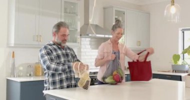 Modern mutfakta erzak paketlerini açmak, olgun bir çiftin gülümsemesi ve konuşması. sohbet, yerli, yaşam tarzı, mutluluk, etkileşim