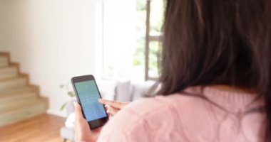 Evdeki akıllı ev ışıklandırmasını kontrol etmek için akıllı telefon uygulaması kullanan bir kadın. Teknoloji, yenilik, ev otomasyonu, bağlantı, dijital, yaşam tarzı
