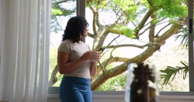 Kadın pencere kenarındaki kahveden zevk alıyor, evde doğa manzaralı rahatlıyor, fotokopi çekiyor. Rahat, rahatlama, yaşam tarzı, huzur, sükunet, evcil