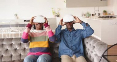 VR kulaklıkları kullanarak, genç Afro-Amerikan çift koltukta oturuyor ve evde sanal gerçekliğin tadını çıkarıyorlar. teknoloji, oyun, eğlence, sürükleyici, rahatlama, dijital