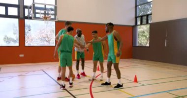 Basketbolcular kapalı spor salonunda koçla salya akıtma eğitimi yapıyorlar. Koçluk, antrenman, sportmenlik, takım çalışması, egzersiz, spor