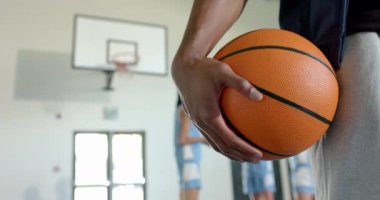 Basketbolu elinde tutan, spor salonunda arka planda takım arkadaşlarıyla duran bir oyuncu. Spor, takım çalışması, sporcular, spor salonu, antrenman, antrenman