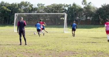 Sahada futbol oynuyorlar, takım üyeleri koşuyor ve kale direğinin yanında pas veriyorlar. Spor, takım çalışması, rekabet, aktif