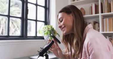 Gülümseyen kadın evinde mikrofon ve dizüstü bilgisayarla podcast yapıyor. Yayın, ev stüdyosu, teknoloji, medya