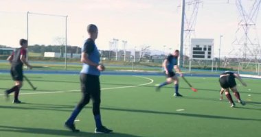 Çim hokeyi oynuyorlar, erkek sporcular açık hava okul sahasında yarışıyorlar. Spor, takım çalışması, rekabet, atletizm