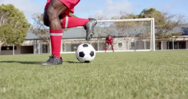 Futbol oynayan, kırmızı giyen Afro-Amerikan erkek sporcu sahada kaleye doğru topa vuruyor, kopyalama alanı. Spor, futbol, yarışma, aksiyon, açık hava, egzersiz