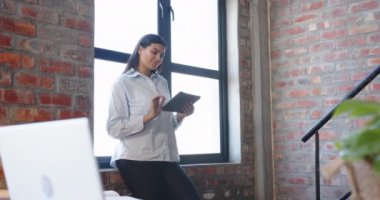 Modern ofiste pencerenin önünde dururken elinde tablet olan gülümseyen kadın. İş, teknoloji, profesyonel, kurumsal, çalışma alanı, dijital