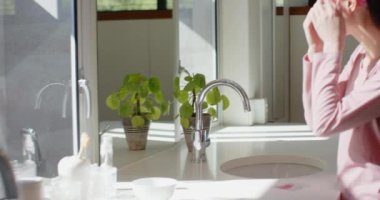 Cilt bakımı, pembe saç bandı takan Asyalı genç kız mutfak lavabosunun yanında bitkiyle bekliyor. Kişisel bakım, güzellik, sağlık, rutin, ev, sabah