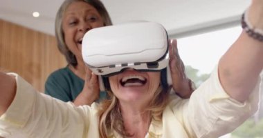 VR kulaklığı kullanarak, evde, oturma odasında arkadaşıyla gülümseyen yaşlı kadın. Sanal gerçeklik, teknoloji, arkadaşlık, mutluluk, boş zaman, kapalı alan