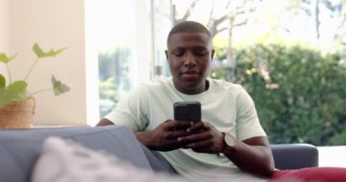 Akıllı telefondan konuşan Afro-Amerikan adam koltukta oturup evde dinleniyor. Teknoloji, iletişim, rahatlık, yaşam tarzı, kapalı alan, konfor