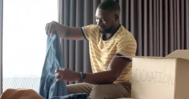 Giysileri bağış kutusuna koyup gülümseyen ve eşyaları düzenleyen Afrikalı Amerikalı bir adam. Hayırseverlik, gönüllü olmak, yardım etmek, vermek, topluluk, değişmemiş, yaşam tarzı