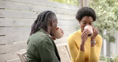 Gülümseyen Afrikalı Amerikalı çift kahveyi birlikte içiyor, terasta bankta oturuyor. Mutlu, gevşeme, bağlanma, sabah, rahat