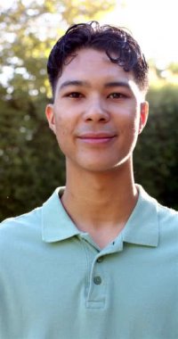 Dikey video: Açık havada gülümseyen genç adam, yeşil gömlek giyiyor, güneşli günün tadını çıkarıyor. Mutluluk, gündelik, yaşam tarzı, gün ışığı, neşe, eğlence