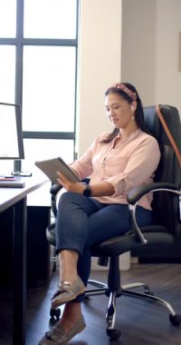 Dikey video: Tablet kullanmak, ofis koltuğunda oturan, modern ofiste çalışan bir kadın. Teknoloji, iş, üretkenlik, meslek, işyeri, şirket