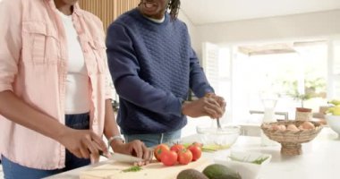 Gülümseyen Afrikalı Amerikalı çift evde yumurta kırıyor ve birlikte yemek hazırlıyorlar. Yemek pişirme, birliktelik, ilişki, aşçılık, ev işi, yaşam tarzı