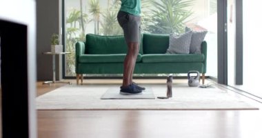 Evde egzersiz yapan, yoga minderinde çömelmiş kettlebell kullanan bir adam. Spor, spor, spor salonu, dayanıklılık eğitimi, egzersiz, değişmemiş, yaşam tarzı.