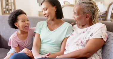 Kanepede oturup, üç nesil boyunca Afro-Amerikan kadınlarının konuşmaları ve gülümsemeleri. Afro-Amerikan ailesi, bağlanma, mutluluk, oturma odası, büyükanne, anne.