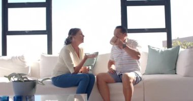 Kanepede oturup, kahve içip içeride sohbet eden yaşlı bir çift. Yaşlı, olgun, rahatlama, oturma odası, bağlanma, boş zaman, değiştirilmemiş, yavaş çekim