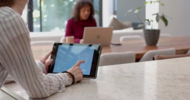 Ev otomasyonu için tablet kullanan arka plandaki kadın dizüstü bilgisayarla çalışıyor. Akıllı ev, teknoloji, dijital, kolaylık, yaşam tarzı, çoklu görev